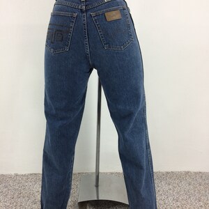 May include: A pair of blue denim jeans with a brown leather patch on the back pocket that says "Wrangler".