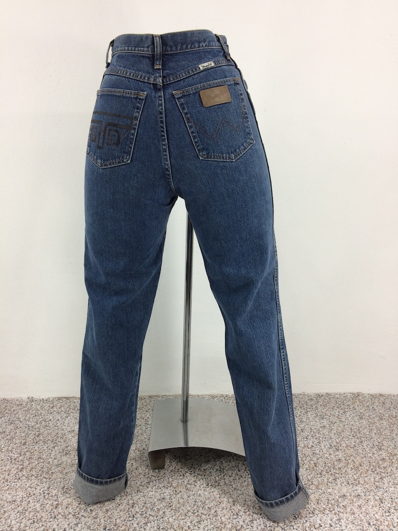 May include: A pair of blue denim jeans with a brown leather patch on the back pocket that says "Wrangler".