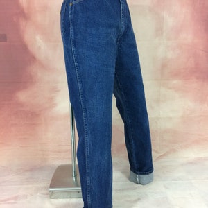 May include: Dark blue denim jeans with a classic straight leg fit. The jeans have a traditional five-pocket design and are cuffed at the ankles. The denim has a medium wash and a slightly faded appearance. The jeans are displayed on a mannequin.