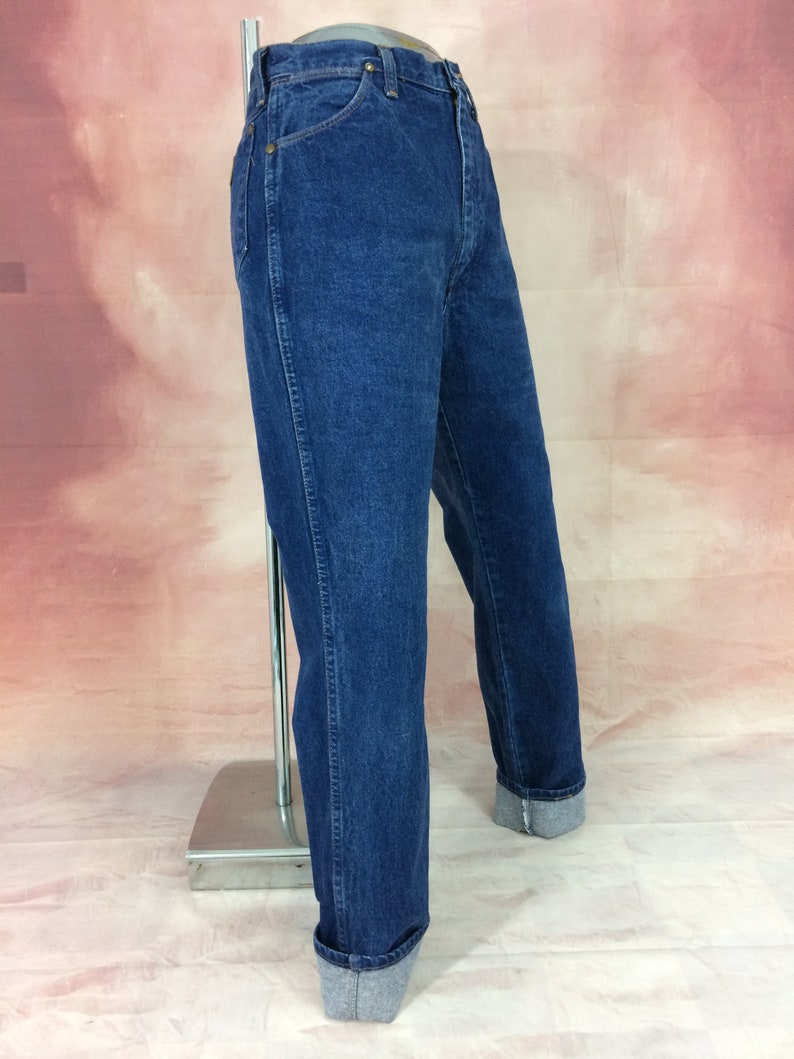 May include: Dark blue denim jeans with a classic straight leg fit. The jeans have a traditional five-pocket design and are cuffed at the ankles. The denim has a medium wash and a slightly faded appearance. The jeans are displayed on a mannequin.