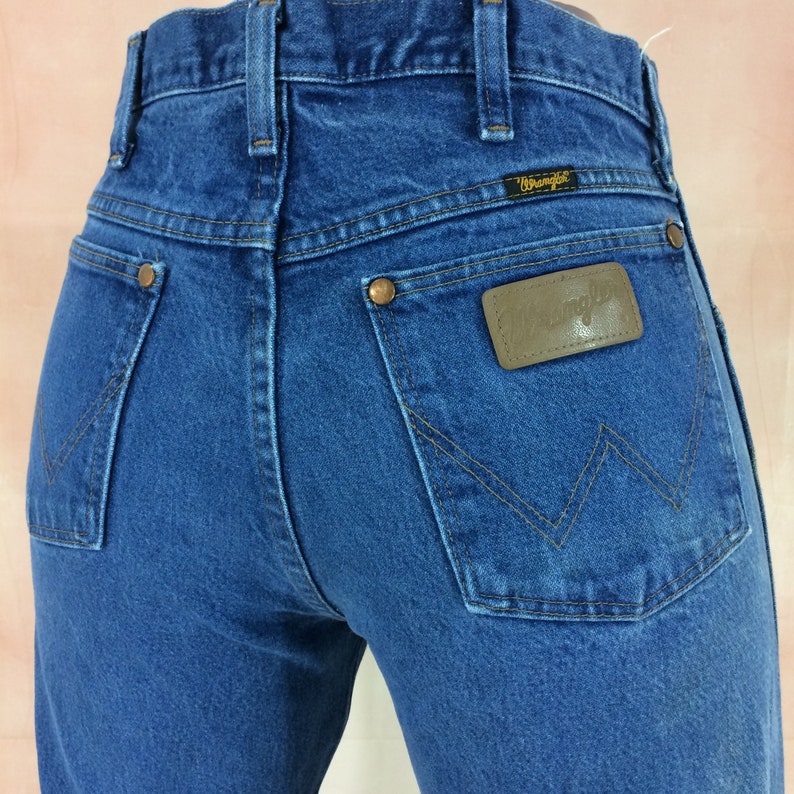 May include: Blue denim jeans with a brown leather Wrangler patch on the back pocket.