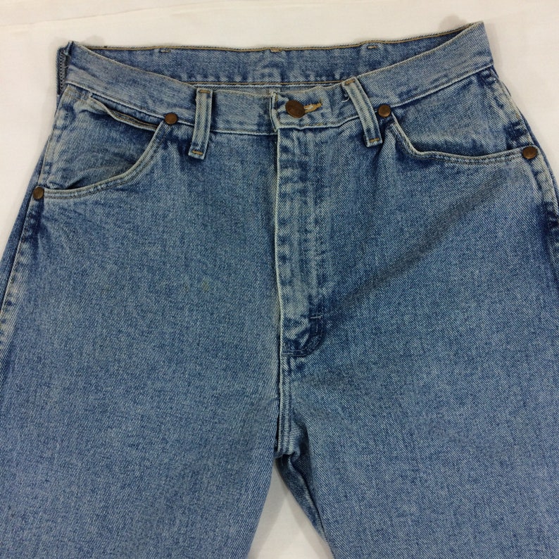 May include: A pair of light blue denim jeans with a high waist and a straight leg. The jeans have a classic five-pocket design and a button fly.