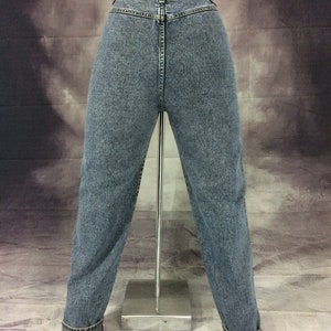 May include: Light blue denim jeans with a classic fit, displayed on a mannequin. The jeans have a high waist, a button and zipper closure, and a cuffed hem. The back pockets are visible, and the denim has a faded wash.