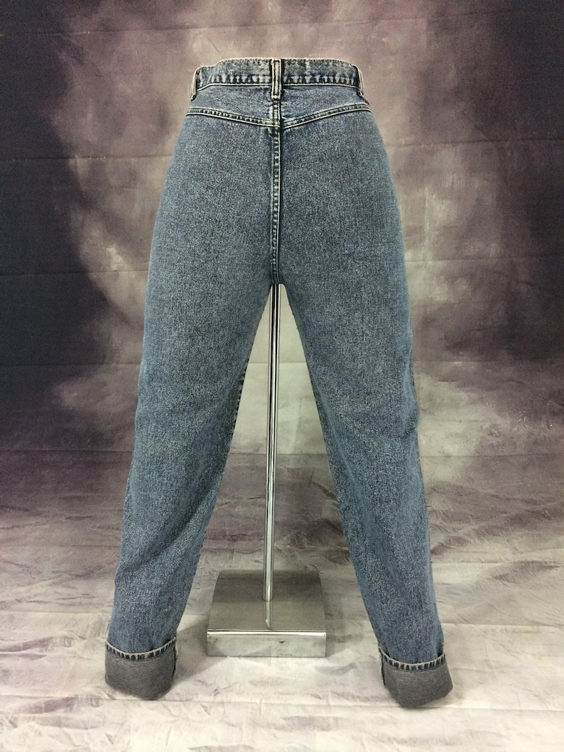 May include: Light blue denim jeans with a classic fit, displayed on a mannequin. The jeans have a high waist, a button and zipper closure, and a cuffed hem. The back pockets are visible, and the denim has a faded wash.