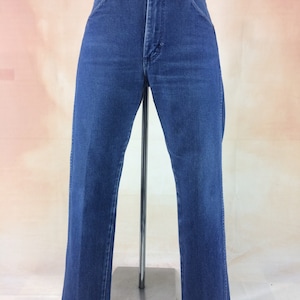 May include: Blue denim jeans with a classic five-pocket design. The jeans have a straight leg cut and a button and zipper closure. The jeans are displayed on a mannequin. The jeans are a medium wash.