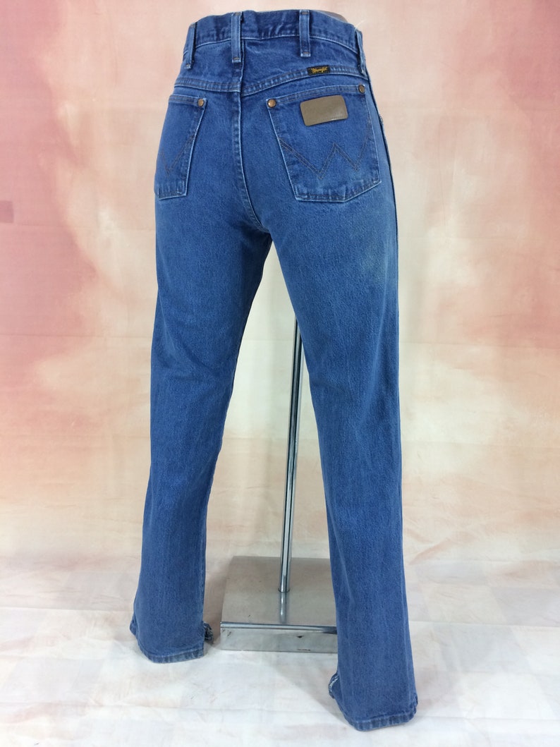 May include: A pair of blue denim jeans with a brown leather patch on the back pocket that says "Wrangler".