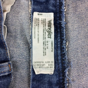 May include: A white care label attached to a pair of blue denim jeans. The label reads "Wrangler 13MWZPW 30 X 34", "Machine wash cold with like colors. Only non-chlorine bleach when needed, tumble dry low or line dry", "Made in Mexico of US fabric, 100% cotton, exclusive of decoration", "RN 130273 1500000260", "70916 LAR-E049-019", "081071128117".