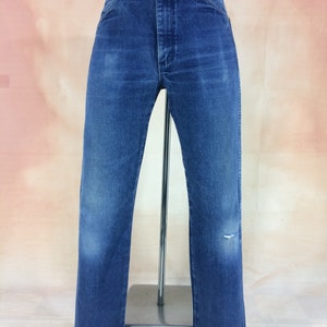 May include: A pair of blue denim jeans with a distressed knee. The jeans have a straight leg and a high waist.