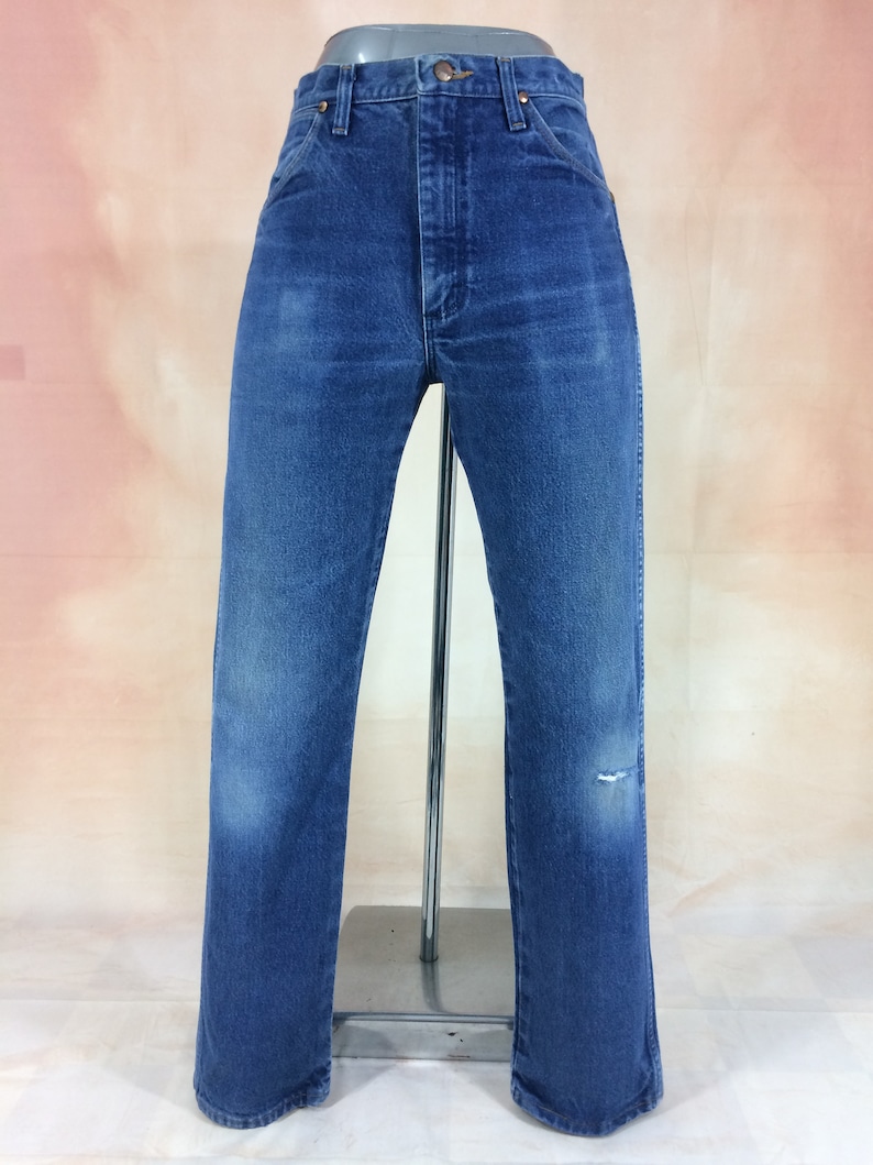 May include: A pair of blue denim jeans with a distressed knee. The jeans have a straight leg and a high waist.