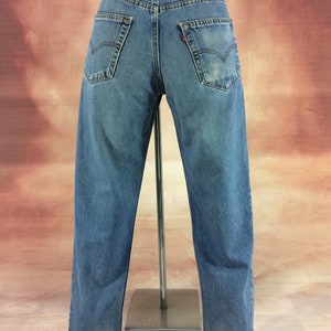 May include: A pair of blue denim jeans with a faded look. The jeans have a straight leg and a high waist. The jeans have a leather patch on the back with the Levi's logo.