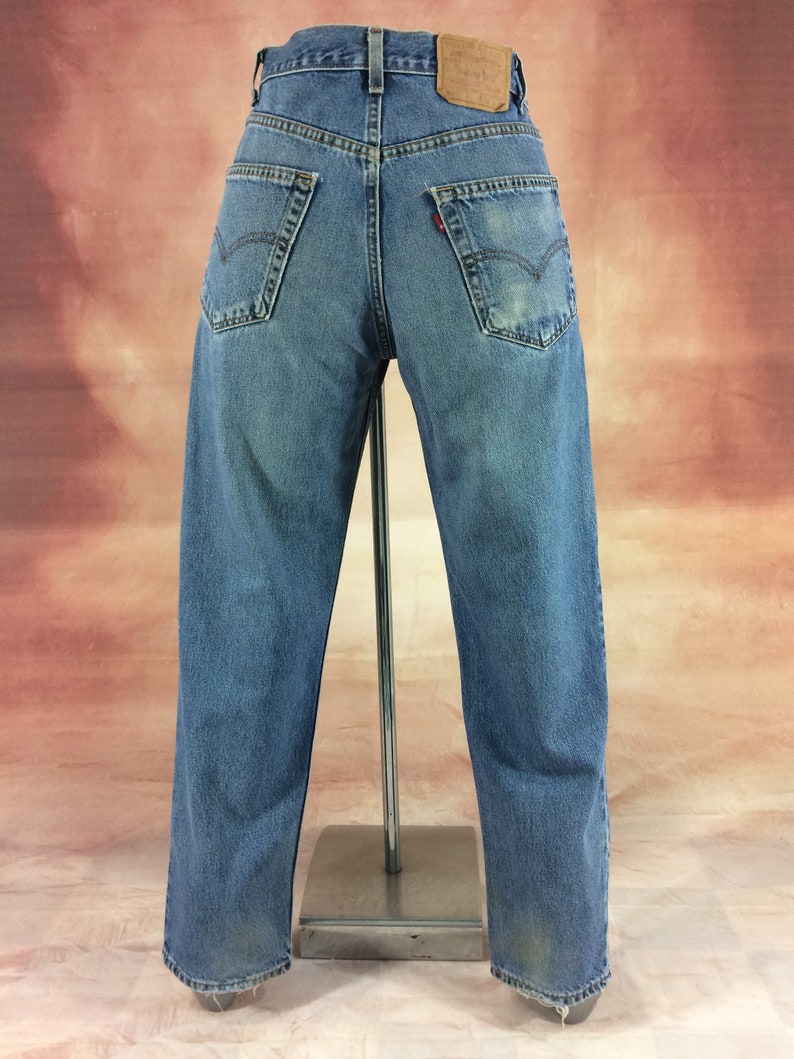 May include: A pair of blue denim jeans with a faded look. The jeans have a straight leg and a high waist. The jeans have a leather patch on the back with the Levi's logo.