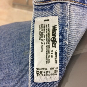 May include: A white Wrangler jeans care label with black text. The label says "Machine wash warm with like colors, only non-chlorine bleach when needed. Tumble dry low. Made in Mexico of US fabric. 100% cotton. Wrangler 14MWZAW 9 X 30"