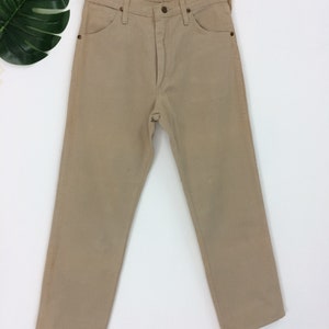 May include: A pair of light brown straight leg jeans hanging on a wooden hanger against a white background.