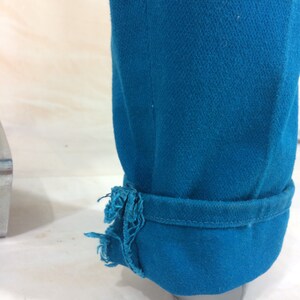 May include: A pair of teal blue jeans with a frayed hem. The jeans are rolled up at the bottom and the fabric is textured.