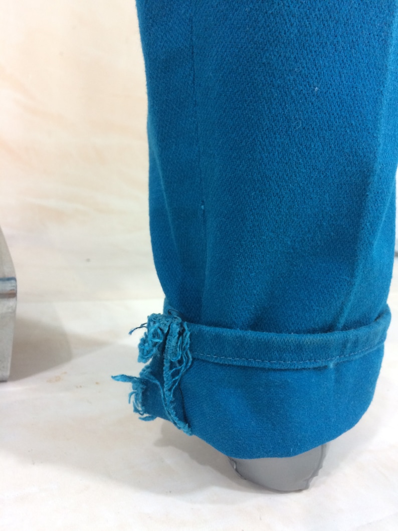 May include: A pair of teal blue jeans with a frayed hem. The jeans are rolled up at the bottom and the fabric is textured.