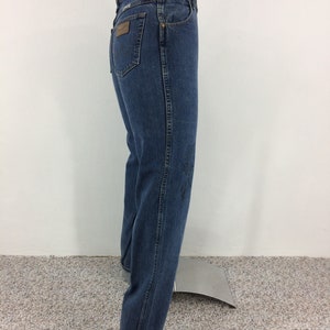 May include: A pair of blue denim jeans with a brown leather patch on the back pocket. The jeans have a straight leg and are cuffed at the bottom.