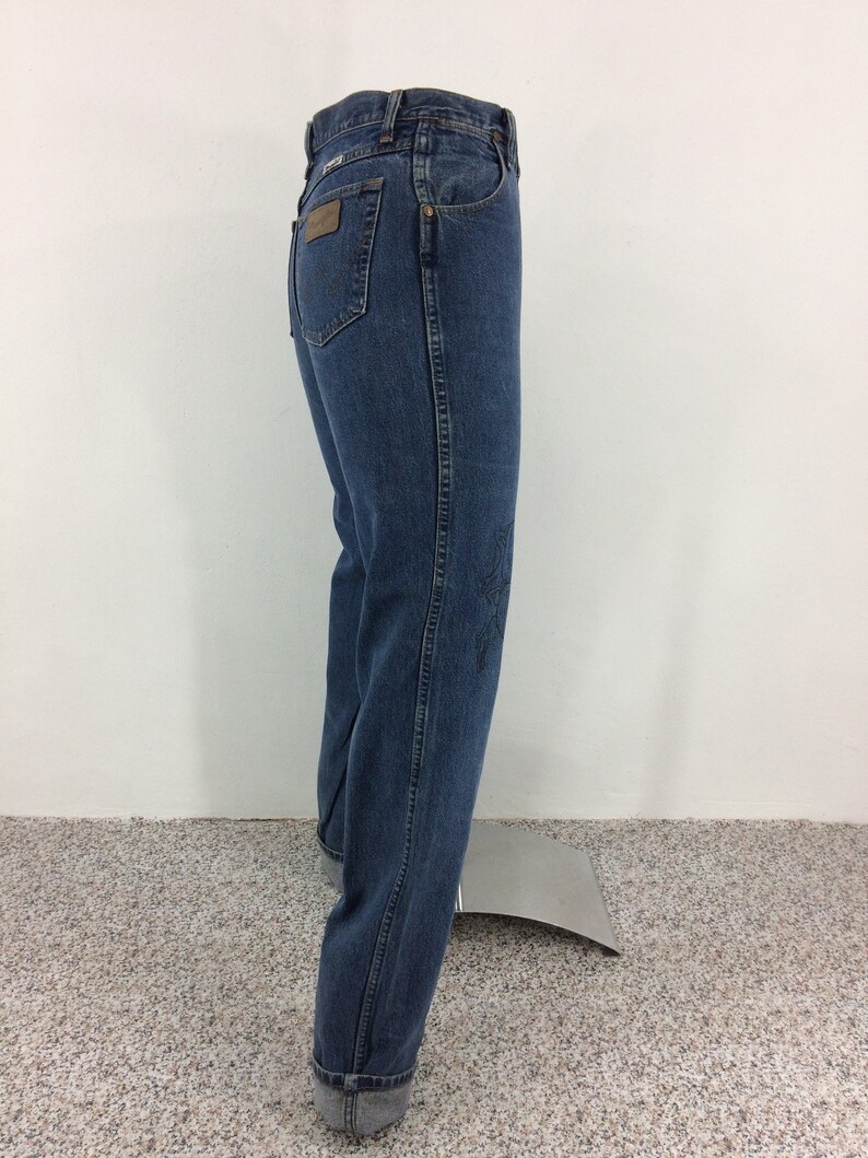 May include: A pair of blue denim jeans with a brown leather patch on the back pocket. The jeans have a straight leg and are cuffed at the bottom.