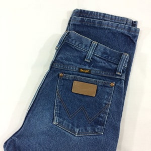 May include: A pair of blue denim jeans folded in half, showing the back pocket with a brown leather patch that says "Wrangler" in gold lettering.