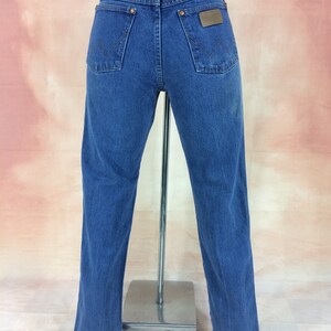 May include: A pair of blue denim jeans with a brown leather patch on the back pocket that says "Wrangler".