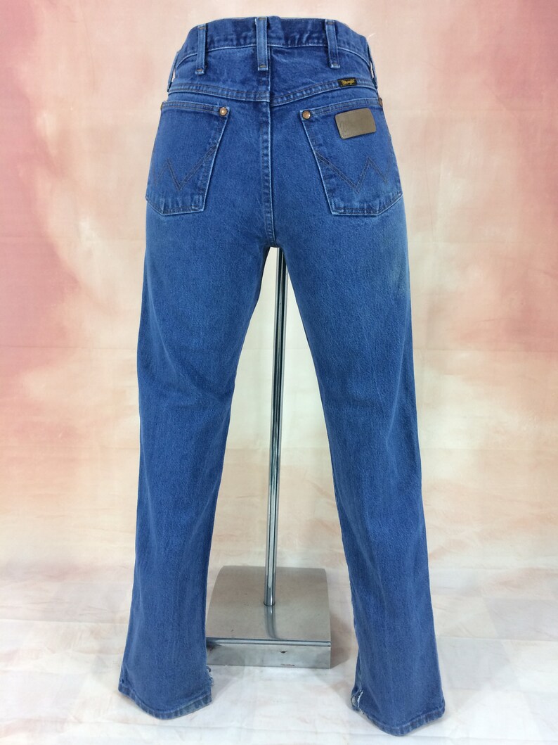 May include: A pair of blue denim jeans with a brown leather patch on the back pocket that says "Wrangler".