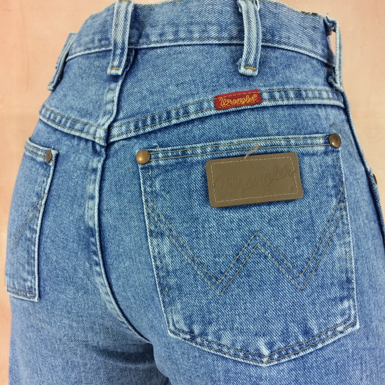 May include: A pair of light blue denim jeans with a brown leather Wrangler label on the back pocket. The jeans have a high waist and a classic straight leg fit.