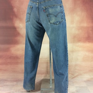 May include: A pair of blue denim jeans with a brown leather patch on the back waistband that says "Levi's" in white text. The jeans have a straight leg and are worn.