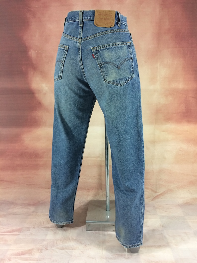 May include: A pair of blue denim jeans with a brown leather patch on the back waistband that says "Levi's" in white text. The jeans have a straight leg and are worn.