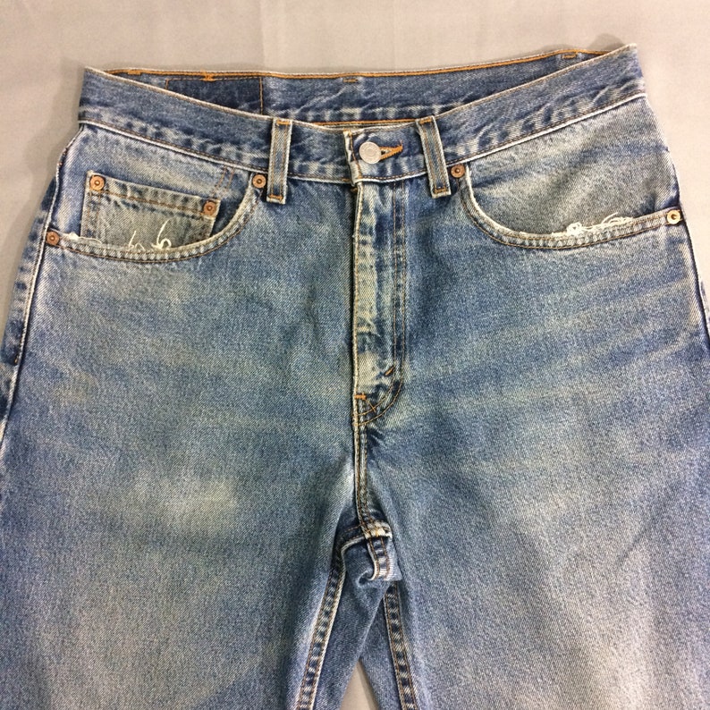 May include: A pair of light blue denim jeans with a faded look. The jeans have a classic five-pocket style and a button fly.