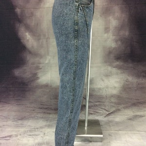 May include: Acid wash denim jeans with a straight leg and cuffed hem. The jeans have a classic five-pocket design and a zipper fly. The denim is a medium wash with a faded, worn look. The jeans are displayed on a mannequin.