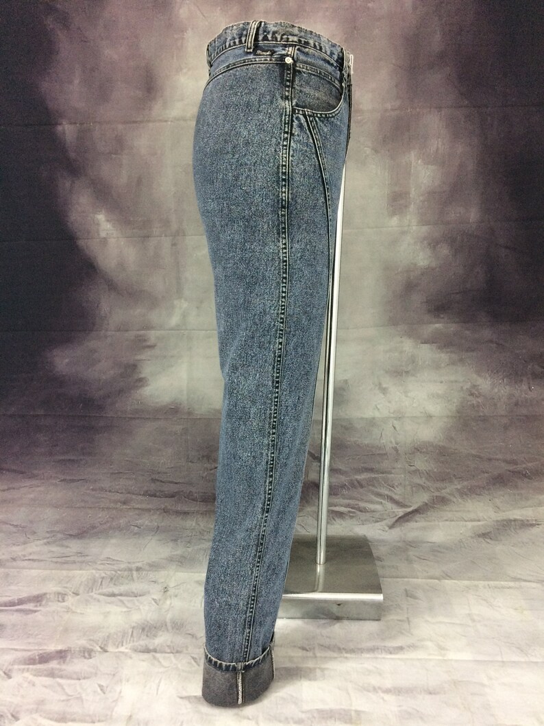 May include: Acid wash denim jeans with a straight leg and cuffed hem. The jeans have a classic five-pocket design and a zipper fly. The denim is a medium wash with a faded, worn look. The jeans are displayed on a mannequin.