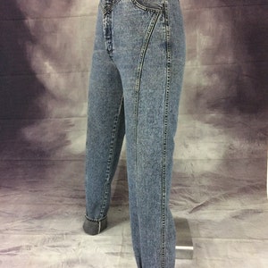 May include: Acid wash denim jeans with a high waist and unique seam detailing. The jeans have a classic five-pocket design and are cuffed at the ankles. The light blue wash and tailored fit give a vintage aesthetic.