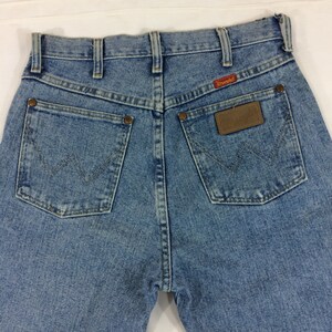 May include: A pair of light blue denim jeans with a brown leather patch on the back pocket that says "Wrangler".
