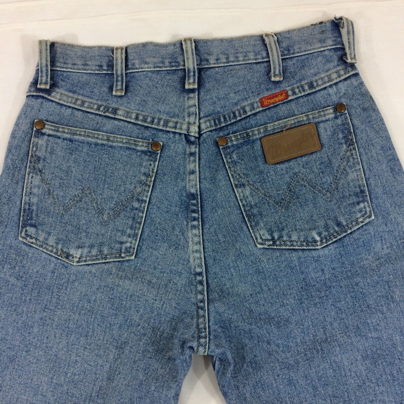 May include: A pair of light blue denim jeans with a brown leather patch on the back pocket that says "Wrangler".