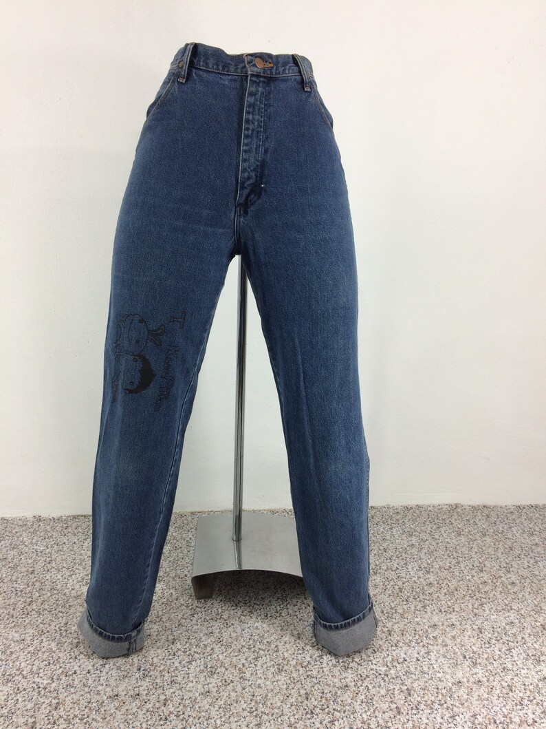 May include: A pair of blue denim jeans with a black graphic on the left leg. The jeans have a high waist and a straight leg fit.