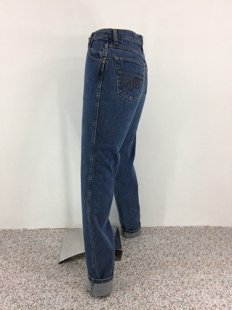 May include: A pair of blue denim jeans with a black embroidered design on the back pocket. The jeans have a high waist and a straight leg.