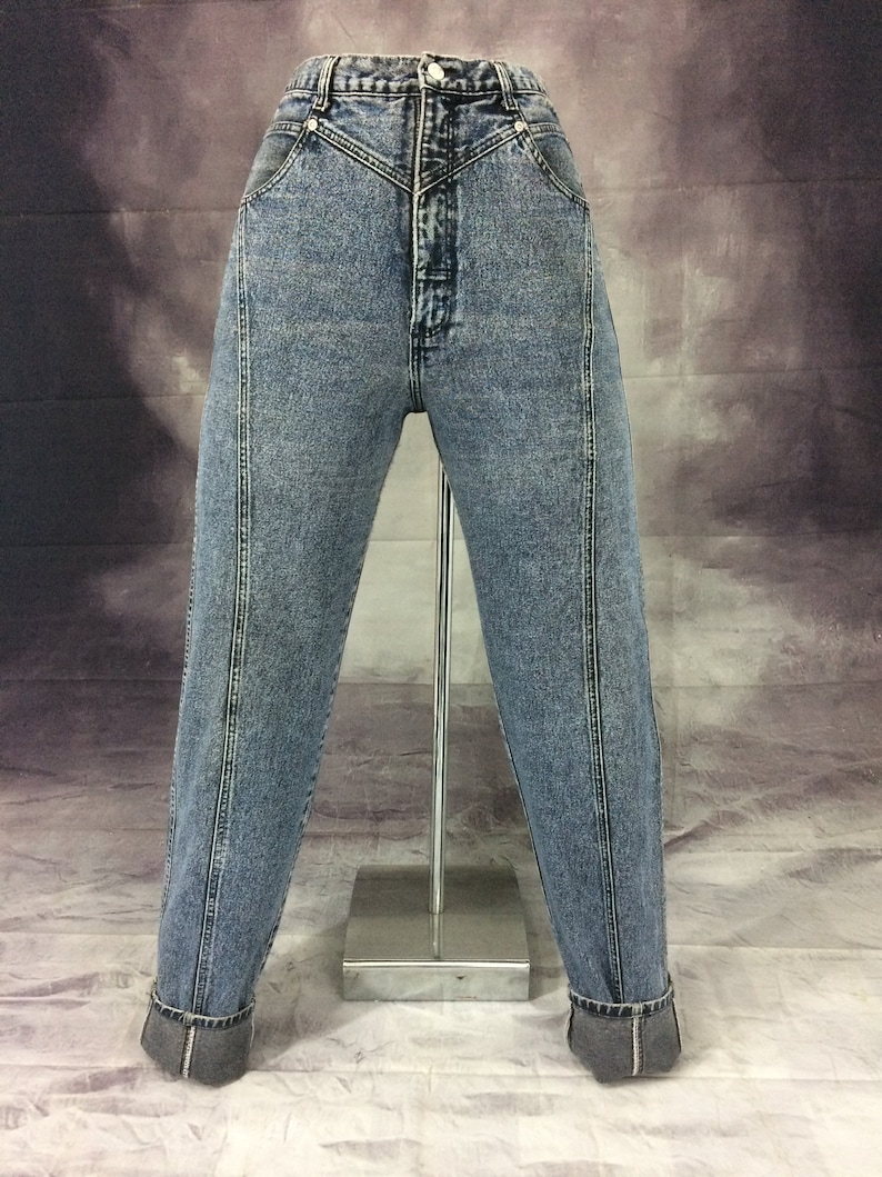 May include: Acid wash denim jeans with a high waist and a button closure. The jeans have a classic five-pocket design and a straight leg with a cuffed hem. The jeans are displayed on a mannequin.