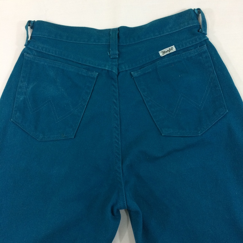 May include: Teal blue denim jeans with a back pocket and a Wrangler label.