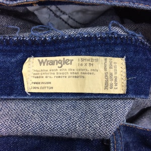 May include: Close-up of blue denim jeans with a Wrangler label. The label indicates the size is 16 x 34 and the material is 100% cotton. The jeans have a classic design and are made in the USA.