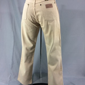 May include: A pair of light brown denim jeans with a brown leather patch on the back pocket that says "Wrangler".