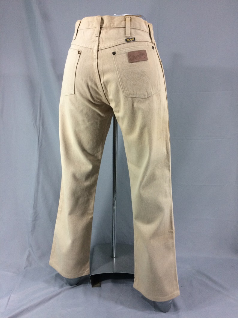May include: A pair of light brown denim jeans with a brown leather patch on the back pocket that says "Wrangler".