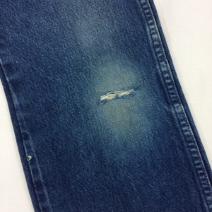 May include: Close-up of a pair of blue denim jeans with a small hole in the knee.