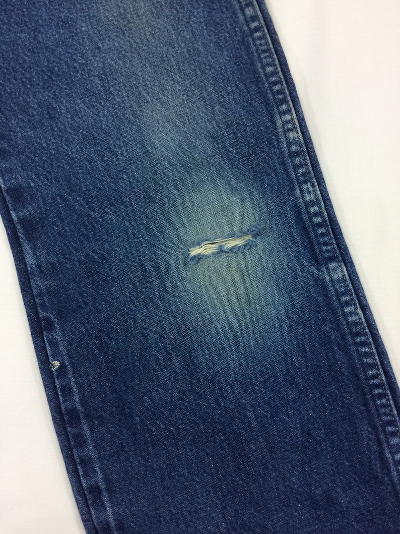 May include: Close-up of a pair of blue denim jeans with a small hole in the knee.