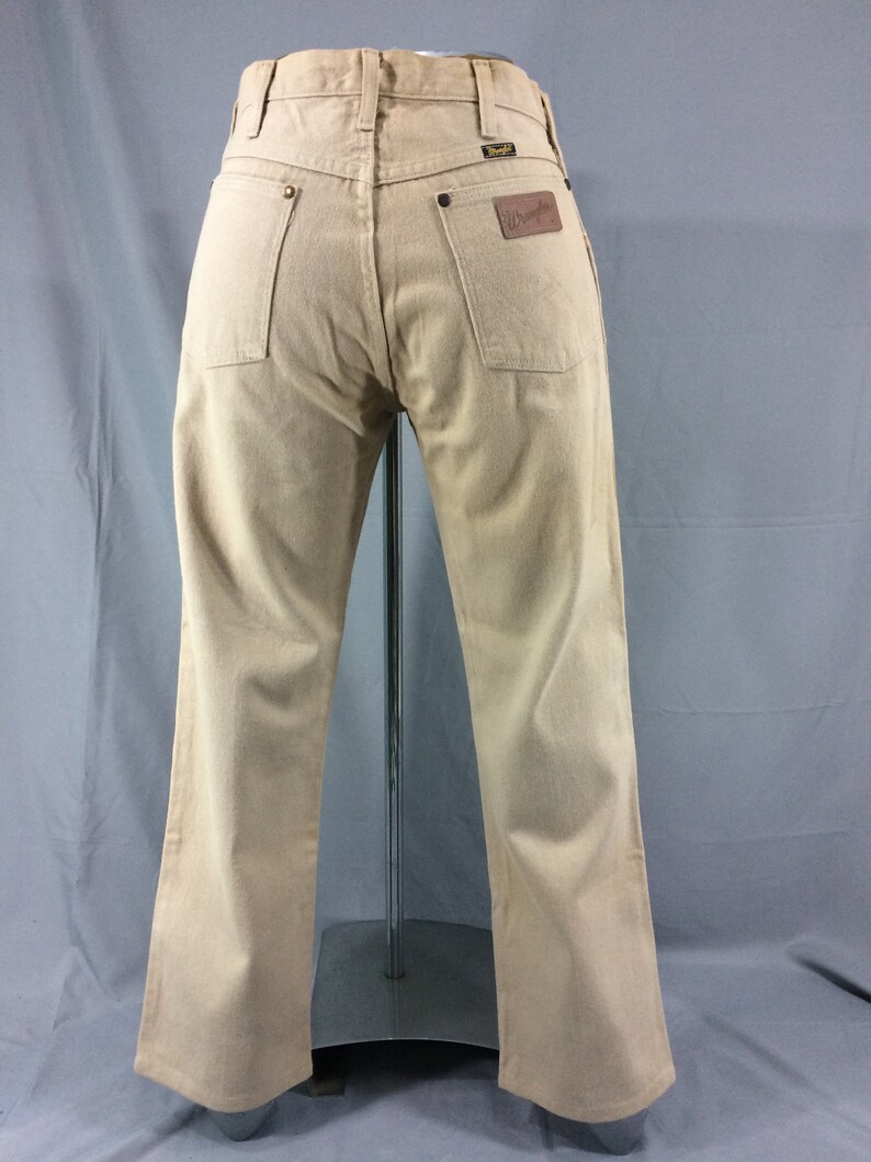 May include: A pair of light brown Wrangler jeans with a brown leather patch on the back pocket.