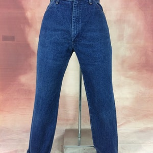 May include: Dark blue denim jeans with a high waist and straight leg. The jeans have a button and zipper closure, belt loops, and a classic five-pocket design. The cuffs are rolled up, revealing a lighter blue interior.