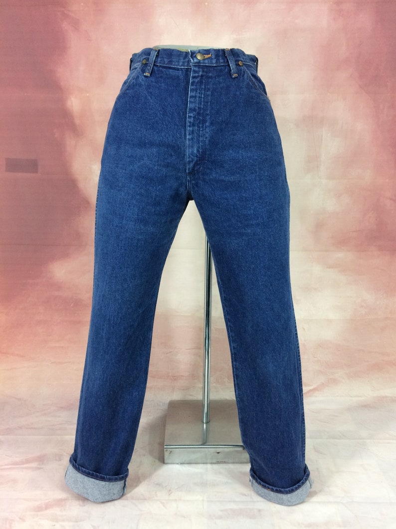 May include: Dark blue denim jeans with a high waist and straight leg. The jeans have a button and zipper closure, belt loops, and a classic five-pocket design. The cuffs are rolled up, revealing a lighter blue interior.
