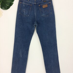 Peut inclure: Un jean bleu en denim avec un &eacute;cusson en cuir marron sur la poche arri&egrave;re qui dit "Wrangler".