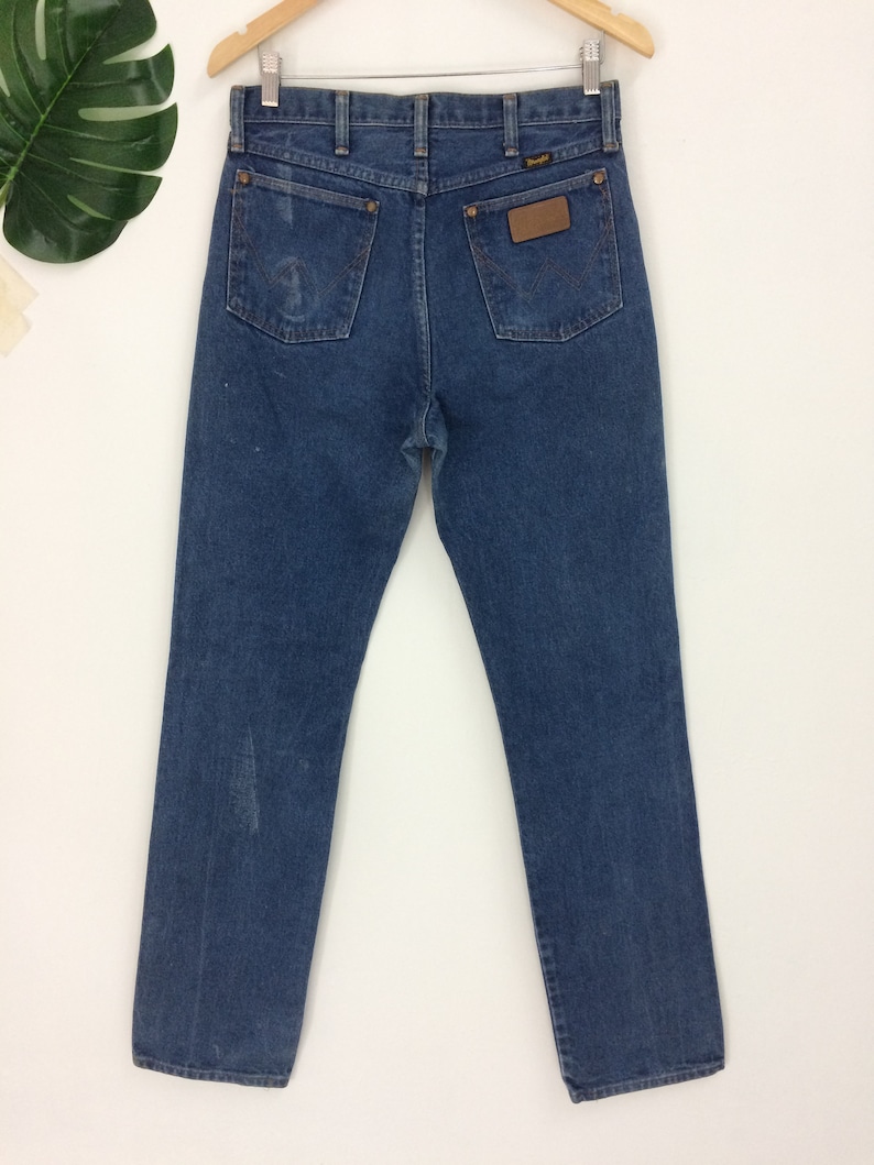 Peut inclure: Un jean bleu en denim avec un &eacute;cusson en cuir marron sur la poche arri&egrave;re qui dit "Wrangler".