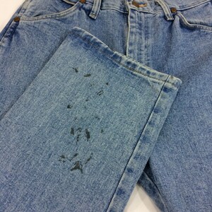 May include: A pair of light blue denim jeans with a faded look. The jeans have a dark stain on the left leg.