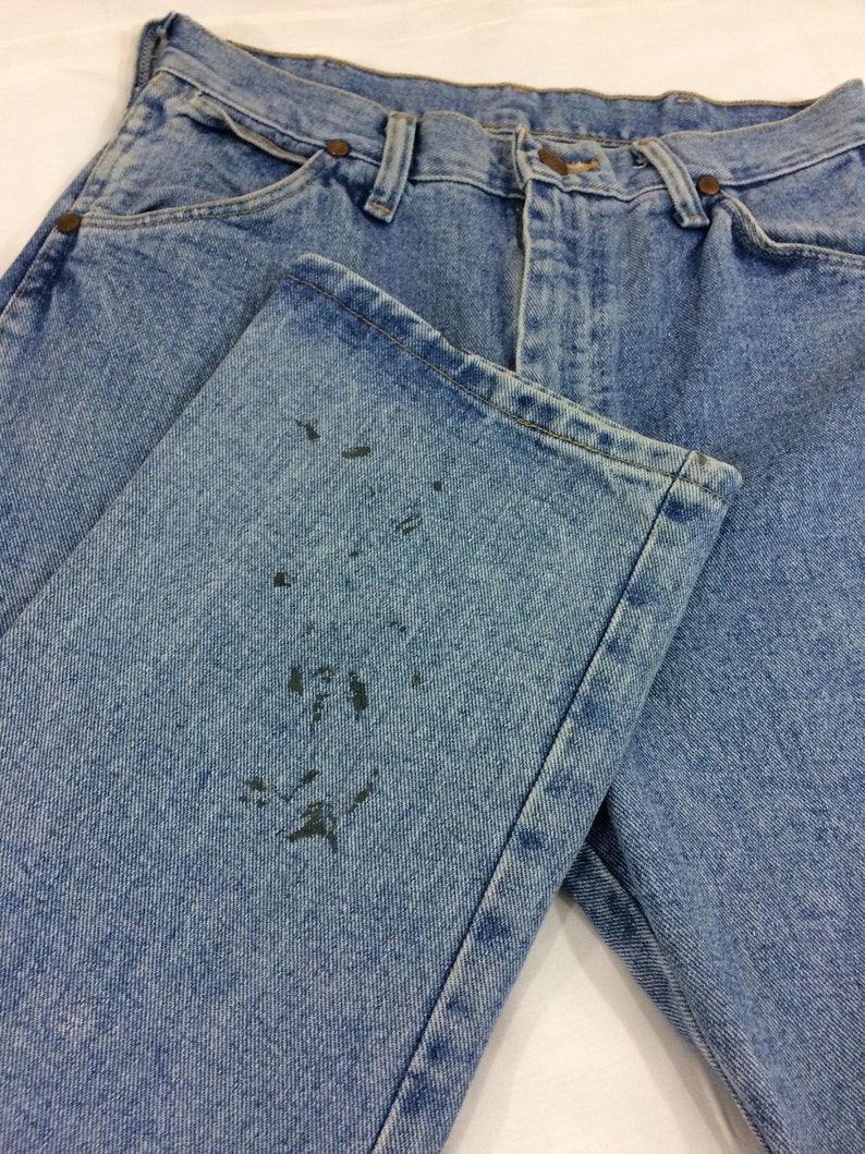 May include: A pair of light blue denim jeans with a faded look. The jeans have a dark stain on the left leg.