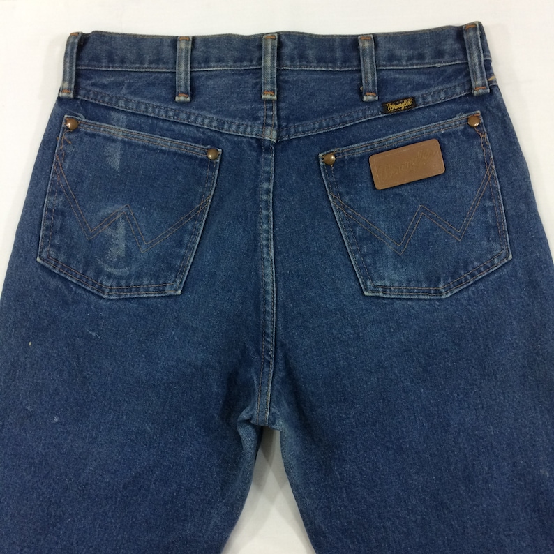 Peut inclure: Un jean bleu denim avec un patch en cuir marron Wrangler sur la poche arri&egrave;re.